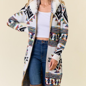 May include: A long, white cardigan with a geometric pattern in black, red, blue, and yellow. The cardigan features a faux fur collar and a zipper closure. The sleeves and hem have a contrasting pattern.