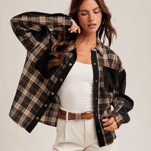 May include: A plaid button-up shirt in brown, black, and tan with black accents. The shirt is worn over a white tank top and paired with white shorts and a brown belt. The outfit is completed with beige cowboy boots.