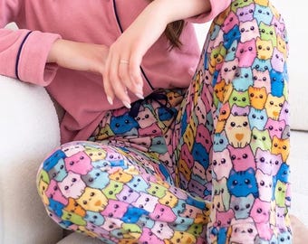 Könnte beinhalten: Ein zweiteiliger Schlafanzug bestehend aus einem einfarbigen, altrosa langärmeligen Oberteil mit Knopfleiste und dunkelblauen Paspeln an Kragen und Ärmelbündchen, kombiniert mit einer locker sitzenden Hose mit buntem Cartoon-Katzenmuster.