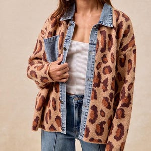 May include: A leopard print jacket in tan and brown with denim detailing. The jacket has a denim collar, pocket, and button closure. The model is wearing a white vest top and blue jeans.