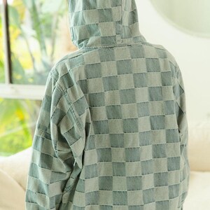 Lightweight denim hoodie with blue and gray checkered pattern, half-zip front, and drawstring hood—perfect for travel, weekend getaways, or road trip layering. Styled with frayed shorts for a relaxed, packable outfit. Keywords: travel hoodie, denim pullover, casual layers, wanderlust wardrobe, easy-to-style essentials.