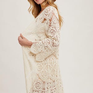 May include: Cream-colored, long-sleeved crochet cardigan with a scalloped hem. The open-front design features intricate floral and geometric patterns. A wide-brimmed brown hat completes the look. This bohemian-style garment is perfect for layering.