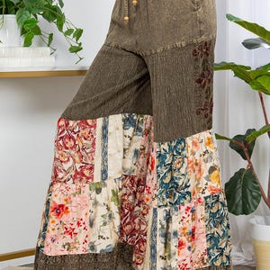 May include: Olive green palazzo trousers with a drawstring waist and floral patchwork design. The trousers feature a wide leg with a lace trim at the hem. The patchwork includes floral patterns in shades of pink, blue, and cream.