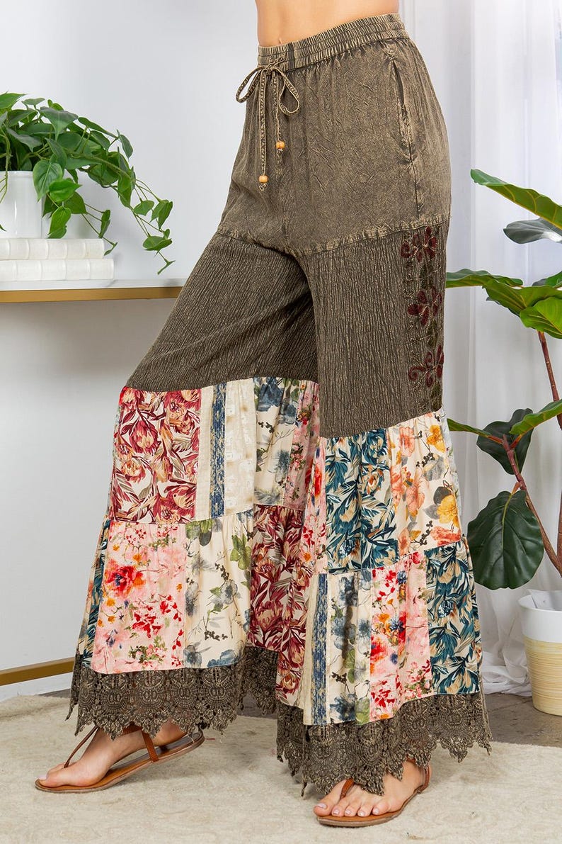May include: Olive green palazzo trousers with a drawstring waist and floral patchwork design. The trousers feature a wide leg with a lace trim at the hem. The patchwork includes floral patterns in shades of pink, blue, and cream.