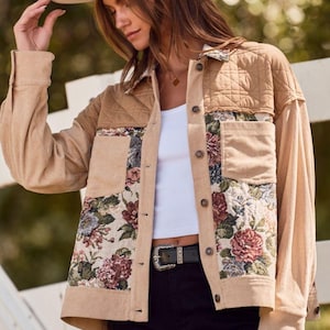 May include: Tan corduroy jacket with floral tapestry panels and quilted shoulder yoke. The jacket features a button-up front, two front pockets, and a collared neckline. A beige fedora hat completes the look.