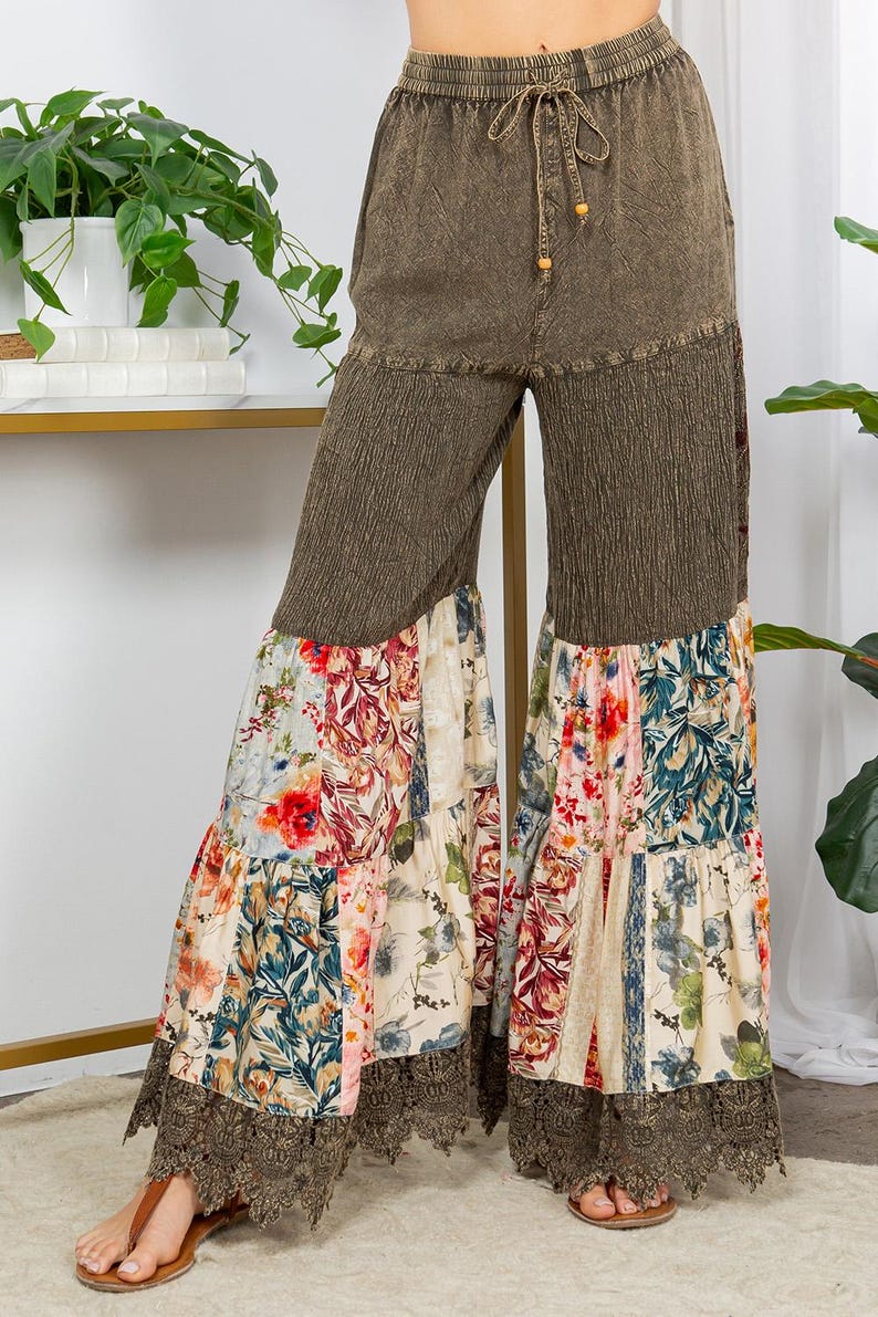 May include: Olive green palazzo trousers with a drawstring waist and floral patchwork design. The trousers feature a wide leg with a floral print and a lace trim at the hem. The fabric has a textured appearance.