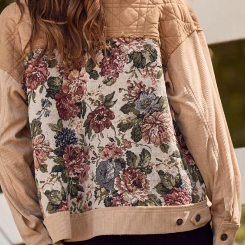 May include: Tan corduroy jacket with a floral tapestry back panel. The jacket features a quilted yoke and corduroy sleeves. The floral pattern includes burgundy, pink, and blue flowers on a cream background. The jacket has a button closure.