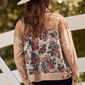 May include: Tan corduroy jacket with a floral tapestry back panel. The jacket features a quilted upper back, buttoned cuffs, and a neutral-toned color palette. A beige hat is worn.
