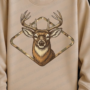 May include: A tan sweatshirt featuring a detailed illustration of a deer's head with large antlers. The deer is framed within a diamond-shaped camouflage pattern. The design is centered on the front of the sweatshirt.