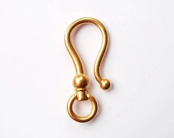 May include: A gold-colored hook clasp, featuring a curved design with a circular ring at the base and a ball at the end of the hook. The clasp is set against a white background.