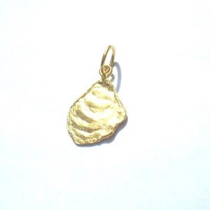 May include: A gold-colored oyster shell pendant with a textured surface and a small loop for a chain. The pendant is a bright, shiny gold color and is set against a white background.