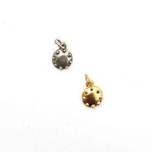 May include: Two small, round charms with a textured surface and a loop for hanging. One charm is silver-colored, and the other is gold-colored. The charms are on a white background.
