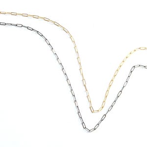 May include: Two delicate chain necklaces. One is gold-colored, the other is a dark gray. Both chains have a paperclip link design. The necklaces are displayed against a white background.