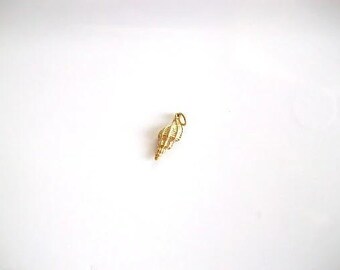 May include: A small, gold-colored seashell charm with a textured surface. The charm is suspended from a small loop, suggesting it can be attached to a necklace or bracelet. The charm is set against a white background.