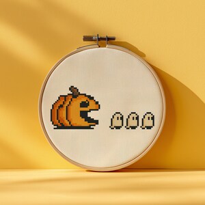 Può includere: Un disegno a punto croce a tema Halloween. Una zucca arancione con una grande bocca aperta insegue tre piccoli fantasmi bianchi. Il disegno è ambientato in un telaio da ricamo in legno, di circa 15 cm di diametro.