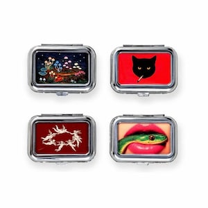 May include: Four rectangular silver pill cases with different designs. One features a mushroom scene, another a black cat with a cigarette on a red background, a third has cherubs, and the last shows a snake in red lips.