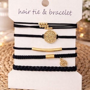 May include: A set of black hair ties and bracelets displayed on a white card. The card reads "hair tie & bracelet". The bracelets feature gold-colored accents, including beads, a circular pendant, and a bar.