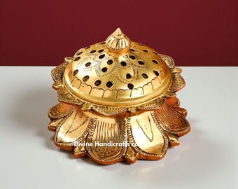 May include: A gold-colored, lotus-shaped incense burner with a lid featuring decorative perforations. The base and lid are adorned with intricate floral patterns. The text "Divine Handicrafts" is visible on the base.