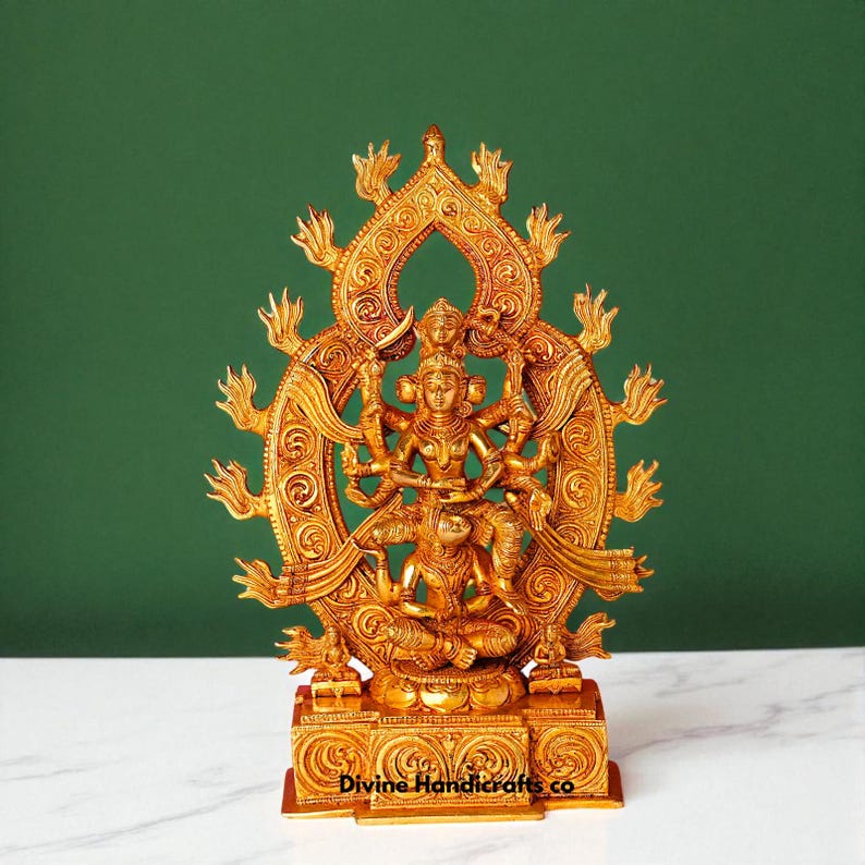 Puede incluir: Una estatua dorada de una deidad con m&uacute;ltiples brazos, sentada en posici&oacute;n meditativa. La estatua es intrincadamente detallada, con patrones ornamentados y una estructura similar a un halo detr&aacute;s de la figura. La base de la estatua tiene el texto "Divine Handicrafts co."