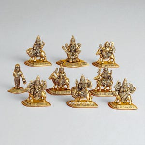 Può includere: Una collezione di piccole statuette religiose color oro. Le statuette raffigurano varie divinità, alcune a cavallo di animali come leoni e cervi. Ogni statuetta poggia su una base con iscrizioni. Il tema generale è religioso e spirituale.