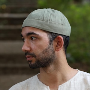 May include: A sage green skull cap with a rounded crown and a stitched brim. The hat is made of a lightweight fabric and has a simple, classic design. This hat is a stylish accessory for casual wear.