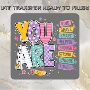 May include: A DTF transfer ready to press featuring the text YOU ARE in colorful patterns, including a yellow pencil, floral, striped, polka dot, and checkered designs. Beside it are labels reading KIND, BRAVE, SMART, HELPFUL, ENOUGH, STRONG, UNIQUE, LOVED.