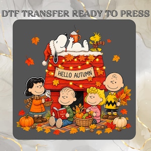 May include: A DTF transfer ready to press featuring a Peanuts cartoon illustration with Snoopy on a red doghouse, Woodstock, and four children. The scene includes autumn leaves, pumpkins, a basket of apples, and a sign that reads HELLO AUTUMN.