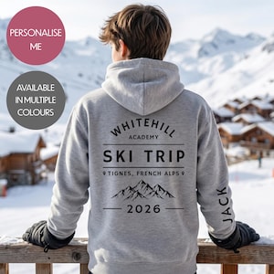 May include: A grey hoodie featuring the text "WHITEHILL ACADEMY SKI TRIP TIGNES, FRENCH ALPS 2026" in black. The name "JACK" is printed on the sleeve. The hoodie is displayed with a snowy mountain and chalet background.