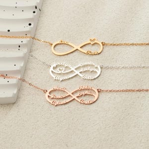 Peut inclure: Trois colliers infinis personnalisés en or, argent et or rose. Chaque collier présente une chaîne et un symbole infini avec des noms gravés. L'un a un charm en forme de cœur.