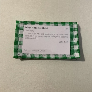 May include: A small, folded card with the text "Must Receive Christ" and a Bible verse from John 1:12. The card is bordered with a green and white checkered pattern.