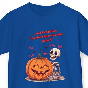 Può includere: T-shirt blu reale con un design a tema Halloween. Il design include una zucca sorridente, uno scheletro e il testo "and he told me, You don't have the guts to do it." con fumetti "HA".