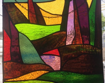 May include: A stained glass window panel with an abstract design featuring a variety of colours, including green, purple, red, and yellow. The panel is framed in black and has a chain hanging from the top.