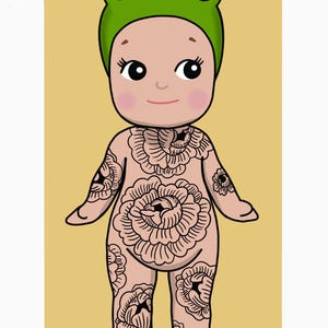 May include: Illustration of a doll wearing a green frog hat with large eyes. The doll has floral tattoos covering its body. The background is a light yellow rectangle against a white background. The doll has rosy cheeks and a small smile.