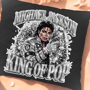 Op de afbeelding: Zwart kussen met een afbeelding van Michael Jackson met de tekst "MICHAEL JACKSON" boven zijn afbeelding en "KING OF POP" eronder. De afbeelding is in zwart-wit met sprankelende accenten.