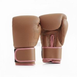 May include: A pair of brown leather boxing gloves with pink trim. The gloves are shown on a white background. The wrist straps have a black closure.