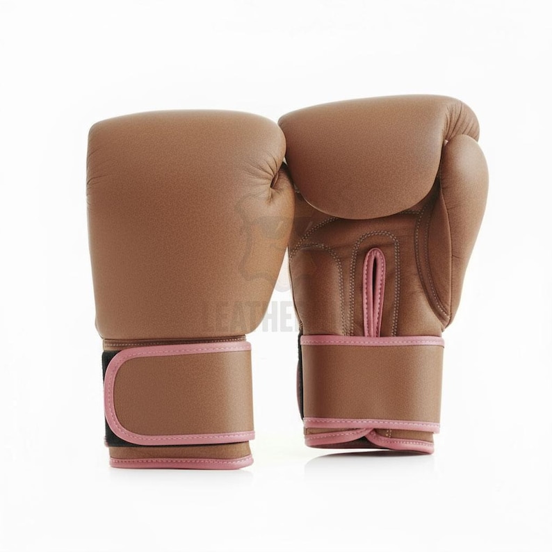 May include: A pair of brown leather boxing gloves with pink trim. The gloves are shown on a white background. The wrist straps have a black closure.