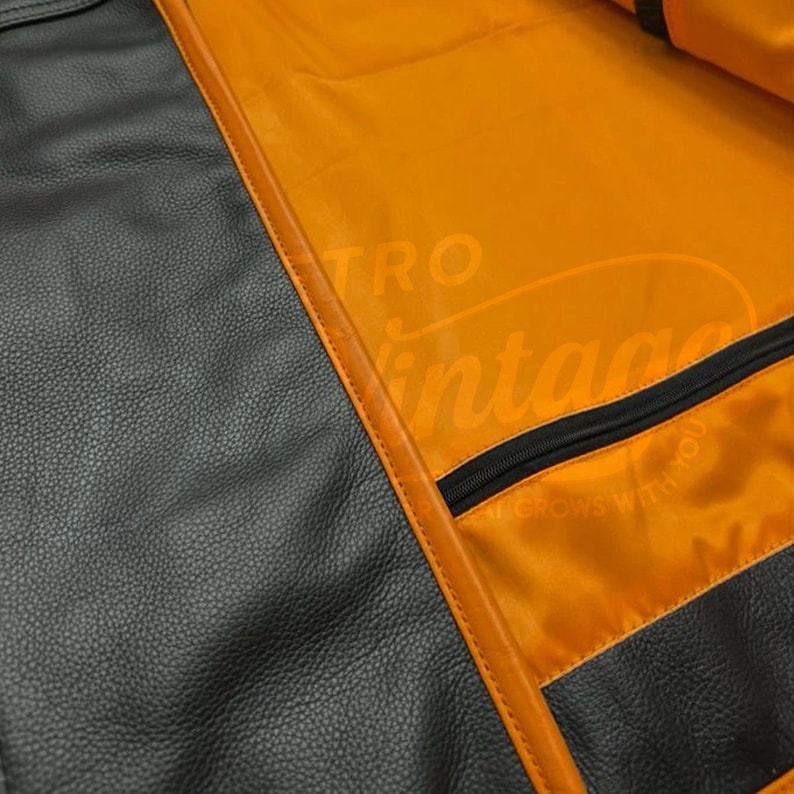 May include: Close-up of a black leather bag with orange lining. The bag has a zipper and is trimmed with orange stitching. The text "TRO Vintage" is visible on the orange lining.