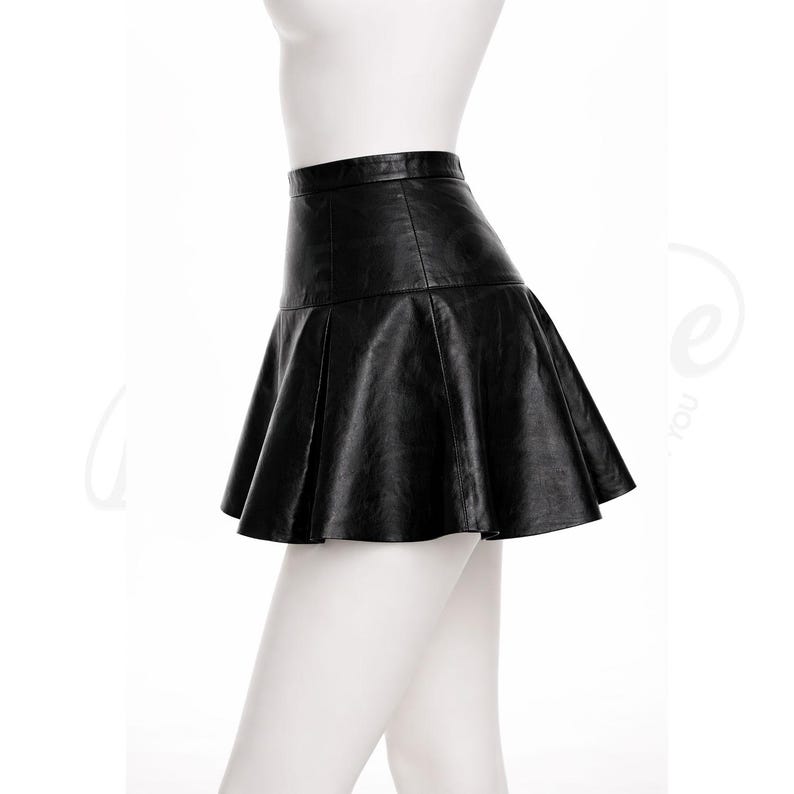 Puede incluir: Minifalda de cuero negro con dise&ntilde;o acampanado y plisado. La falda se muestra sobre un maniqu&iacute; sobre un fondo blanco. La falda tiene una cintura alta y un dobladillo corto y coqueto.