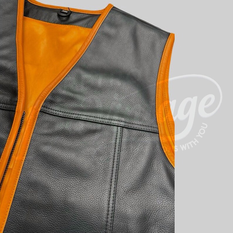 May include: Close-up of a black leather vest with orange trim and lining. The vest has a zipper closure and a classic design. The orange trim outlines the edges of the vest, creating a striking contrast.