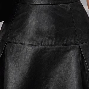 Puede incluir: Primer plano de una falda de cuero negro. La falda tiene una superficie texturizada y un ligero brillo. Los pliegues son visibles y el dise&ntilde;o general es elegante y moderno. El texto "LEATHER MATTERS" es visible.