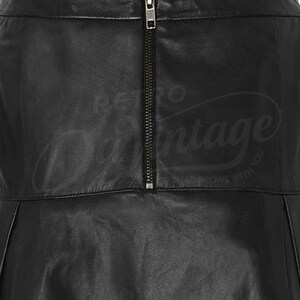 Puede incluir: Primer plano de una falda de cuero negro con cremallera vertical. La falda tiene un dise&ntilde;o plisado y un brillo sutil. El texto "Retro Vintage" es visible en el fondo.
