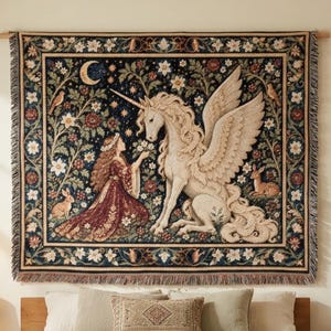 May include: A rectangular woven wall tapestry featuring a central scene of a person with long hair kneeling before a white winged unicorn. The dark background includes a crescent moon, stars, flowers, and small animals within a floral border.