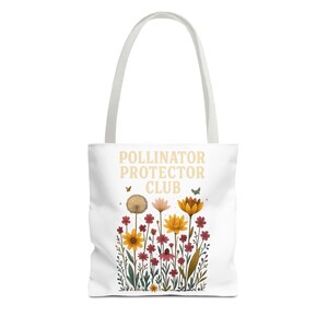 May include: White tote bag with a floral design and the text "POLLINATOR PROTECTOR CLUB". The design features colorful flowers in shades of yellow, red, and pink, with green leaves and small butterflies. The bag has white handles.