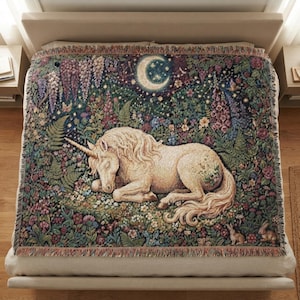 May include: A woven throw blanket featuring a cream-colored unicorn resting in a lush garden filled with colorful flowers, ferns, and greenery. Above the unicorn, a crescent moon and stars are depicted against a dark, deep blue night sky.