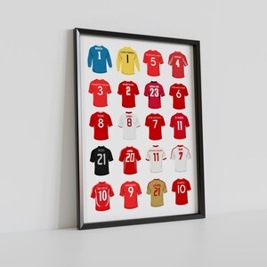 May include: A framed print displaying a selection of football shirts in red, blue, yellow, and black. Each shirt has a number and player's name. The shirts are arranged in a grid within a black frame, suitable for a sports fan.