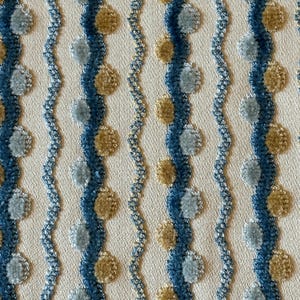 May include: Close-up of a cream-colored fabric with a repeating pattern of vertical blue stripes and wavy lines. The stripes are punctuated by alternating light blue and tan circular tufts, creating a textured, decorative design.