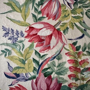 May include: Close-up of a floral fabric featuring large, red and pink flowers with white accents. Green and yellow leaves and blue accents surround the flowers. The background is a light beige color.