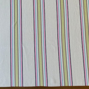 May include: A fabric with vertical stripes in various colors. The stripes include light pink, light blue, green, gray, white, and dark purple. The background is a light beige color. The fabric is likely used for home decor or clothing.