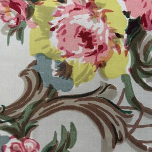 Puede incluir: Primer plano de una tela floral con un patrón repetitivo. El diseño presenta grandes flores estilizadas en tonos rosa, amarillo y rojo, sobre un fondo claro. Hojas verdes y volutas marrones añaden detalles al diseño.