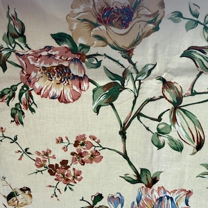 Könnte beinhalten: Nahaufnahme eines floralen Stoffes mit großen, detaillierten Blumen in Rosa, Beige und Blau, mit grünen Blättern und Stielen. Der Stoff hat einen cremefarbenen Hintergrund und erzeugt eine Vintage-Ästhetik. Das Design umfasst kleinere rosa Blüten und einen Vogel.